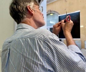 A grey haired man in a striped button up shit etching an x-ray