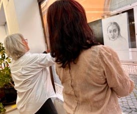 Two women, one grey haired in a white blouse and the other with dark red hair and a cream colored blouse.
